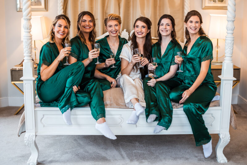 A group of bridesmaids in green pajamas sitting on a bed.