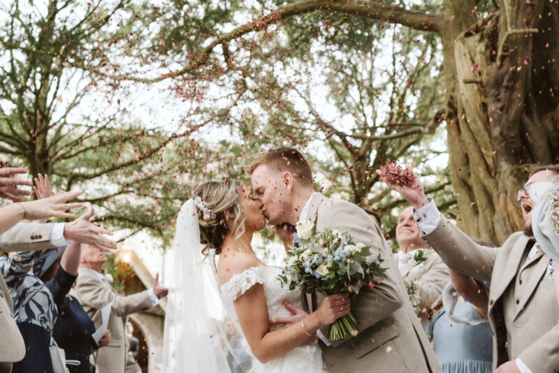 A bride and groom kissing in front of confetti.