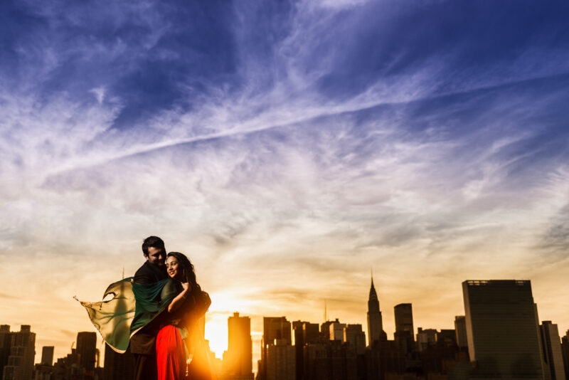 A couple standing in front of a city skyline at sunset.