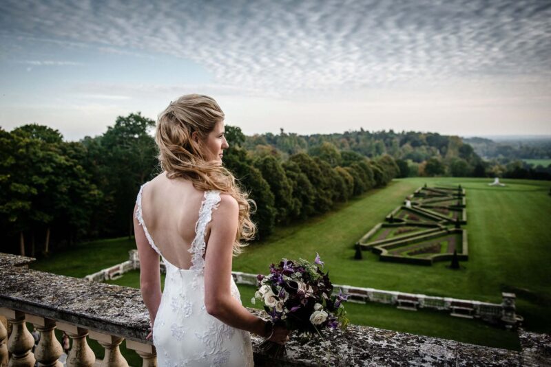 A bride in a wedding dress standing on a balcony overlooking a field.