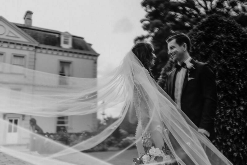 A bride and groom standing in front of a house with a veil.