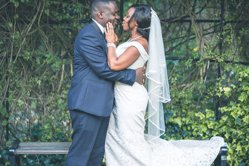 A bride and groom embracing on a bench in a garden.