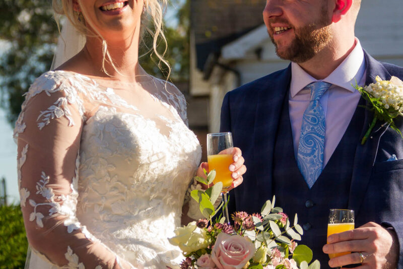 A bride and groom holding champagne glasses in front of a house.