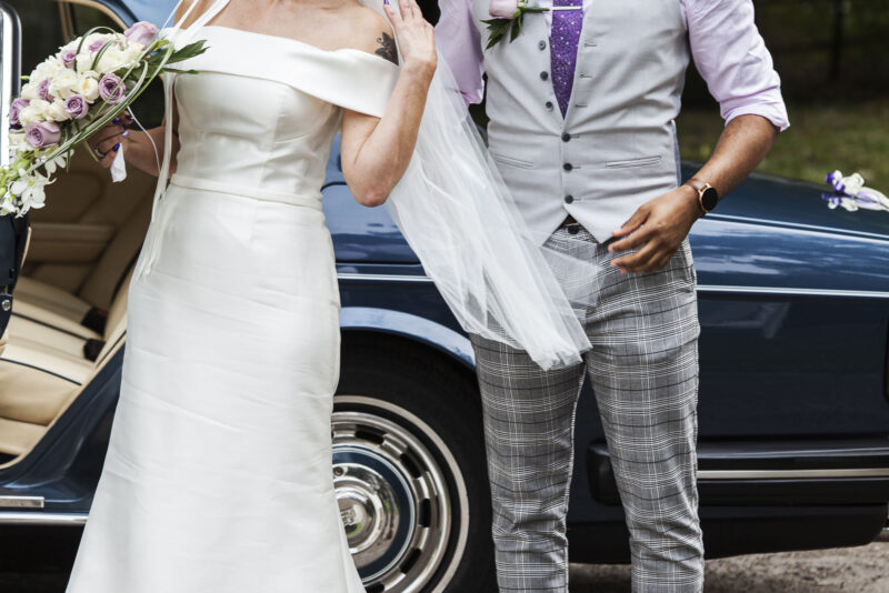 A bride and groom standing next to a blue car.