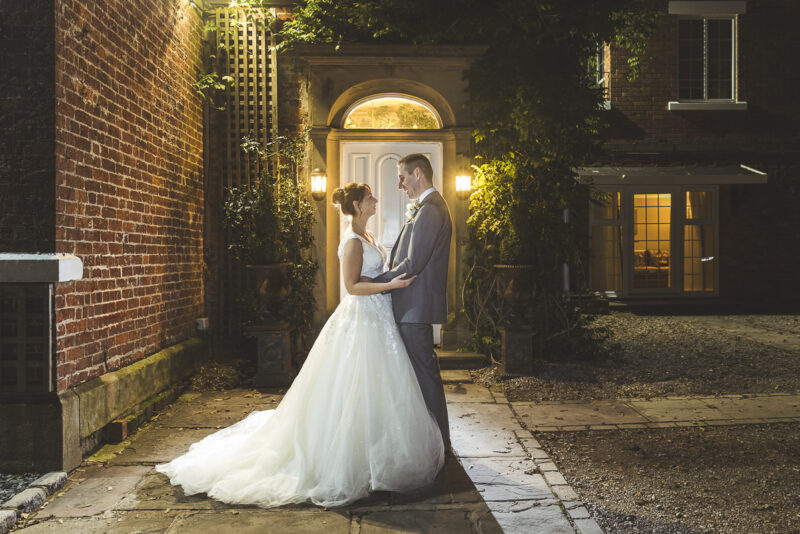 A bride and groom standing in front of a brick building at night.