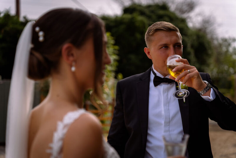 A bride and groom drinking a glass of beer.