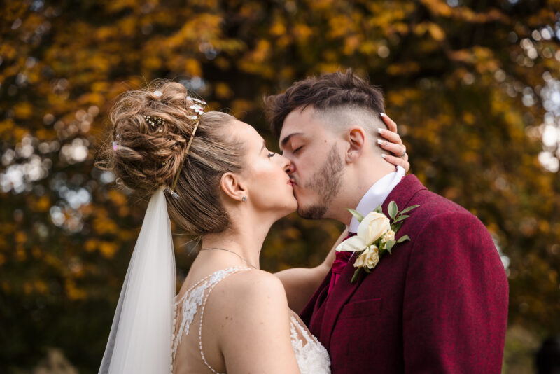 A bride and groom kissing in the autumn leaves.