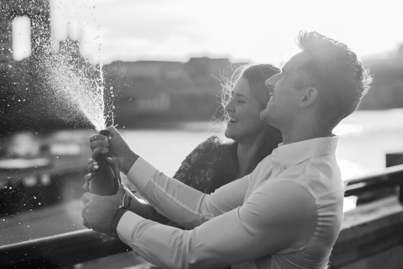 A black and white photo of a couple holding a bottle of champagne.